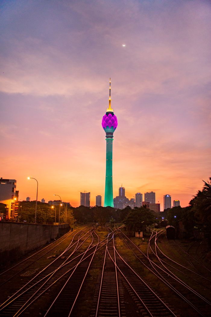 View of illuminated Colombo Lotus Tower at sunset with railway foreground in Sri Lanka.