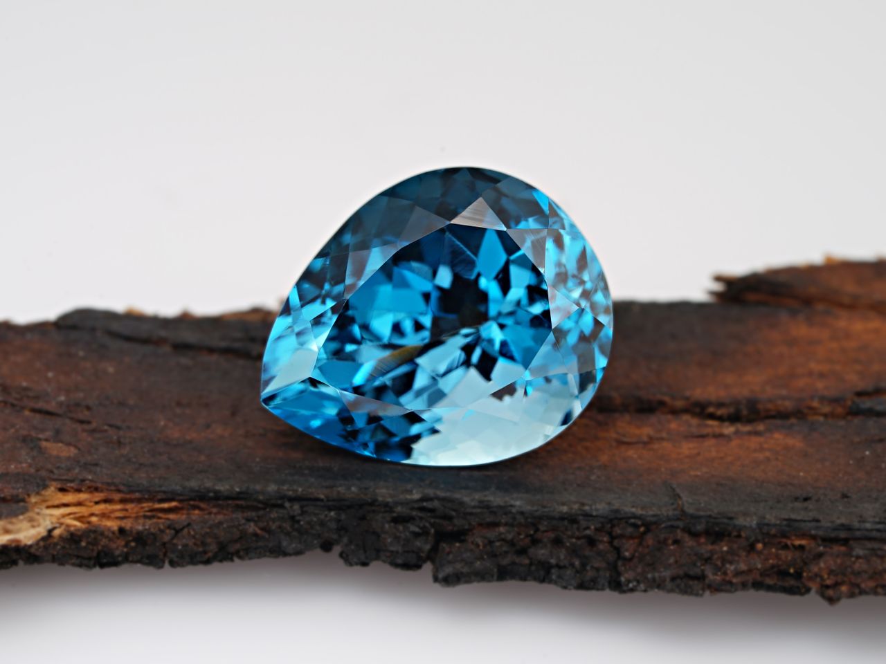 services-06 Stunning close-up of a blue topaz gemstone resting on rustic wood, showcasing its crystal clarity and elegance.