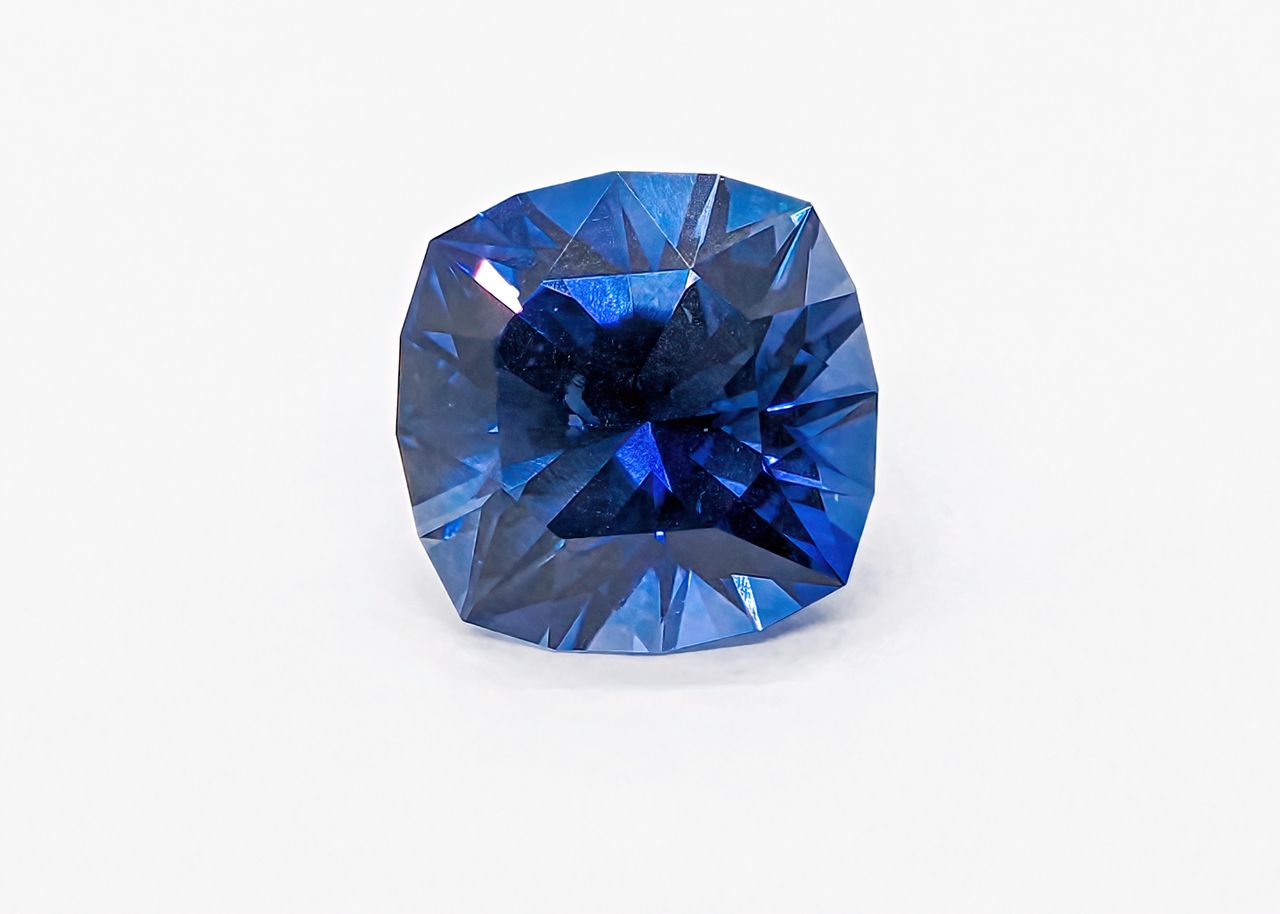 services-05 A vivid blue sapphire gemstone on a white background, showing its intricate facets.